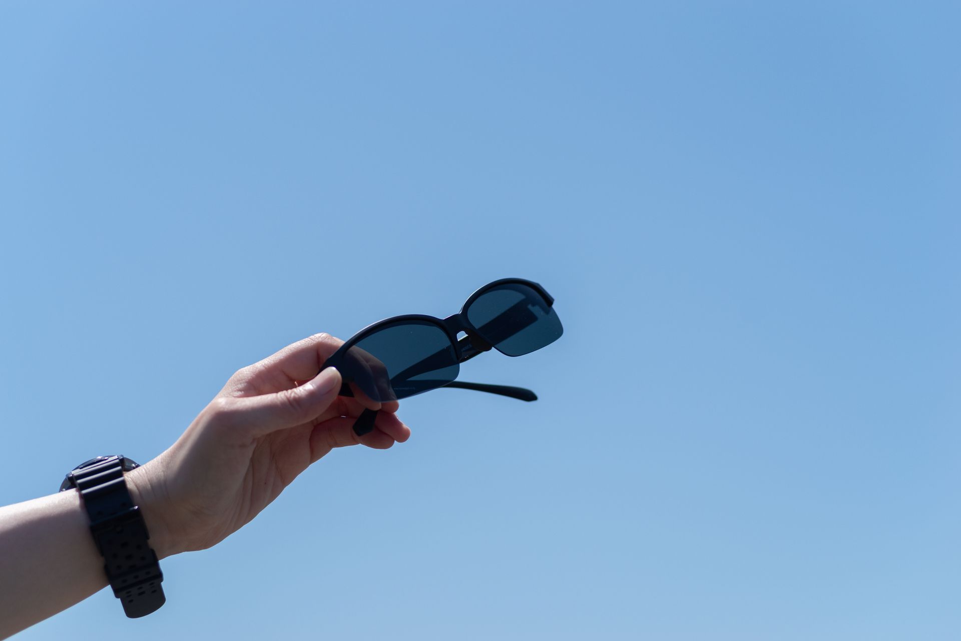 Hand holding sunglasses against a blue sky. Hand holding sunglasses against a blue sky.