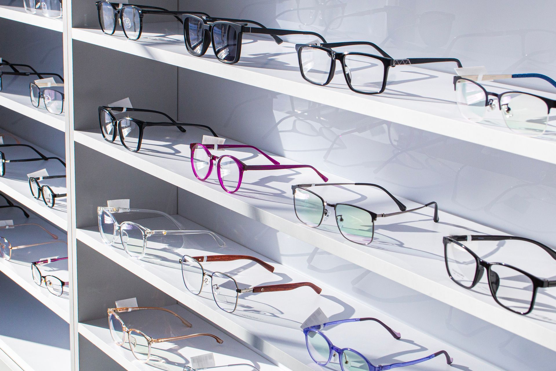 Eyeglasses on white shelves in a store, various styles and colors displayed. Eyeglasses on white shelves in a store, various styles and colors displayed.