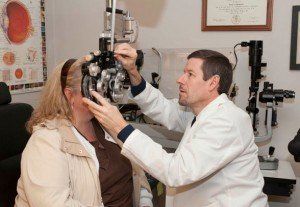 Optometrist examining a patient's eyes with a phoropter in an exam room. Optometrist examining a patient's eyes with a phoropter in an exam room.