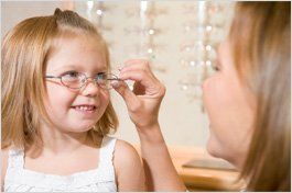 Young child smiles as an adult adjusts her new eyeglasses in an optometry office. Young child smiles as an adult adjusts her new eyeglasses in an optometry office.