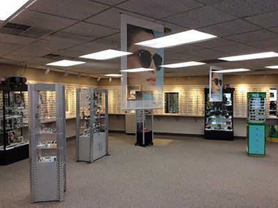 Interior of an optical shop with eyeglasses displays. Displays feature various frames, neutral colors, and fluorescent lighting.