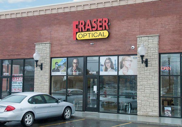 Fraser Optical store exterior with illuminated sign. A silver car is parked in front of the brick building.