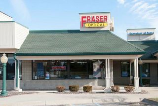 Fraser Optical storefront with a green roof, tan facade, and sign with red and yellow lettering.