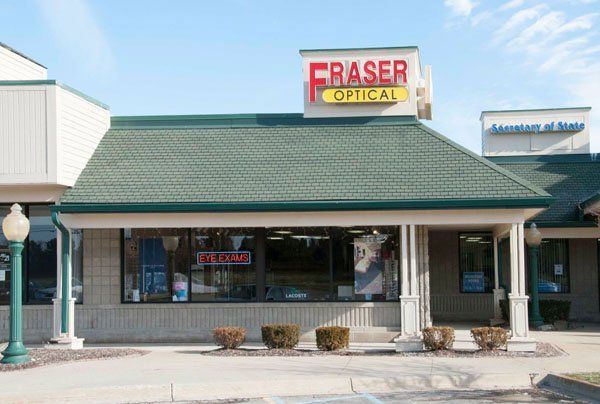 Fraser Optical storefront with a green roof, tan facade, and sign with red and yellow lettering.