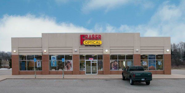 Fraser Optical storefront with tan and brown exterior, windows, and a dark green truck parked in front.