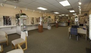 Optical shop interior, eyeglasses displayed on shelves, seating area, and staff area.