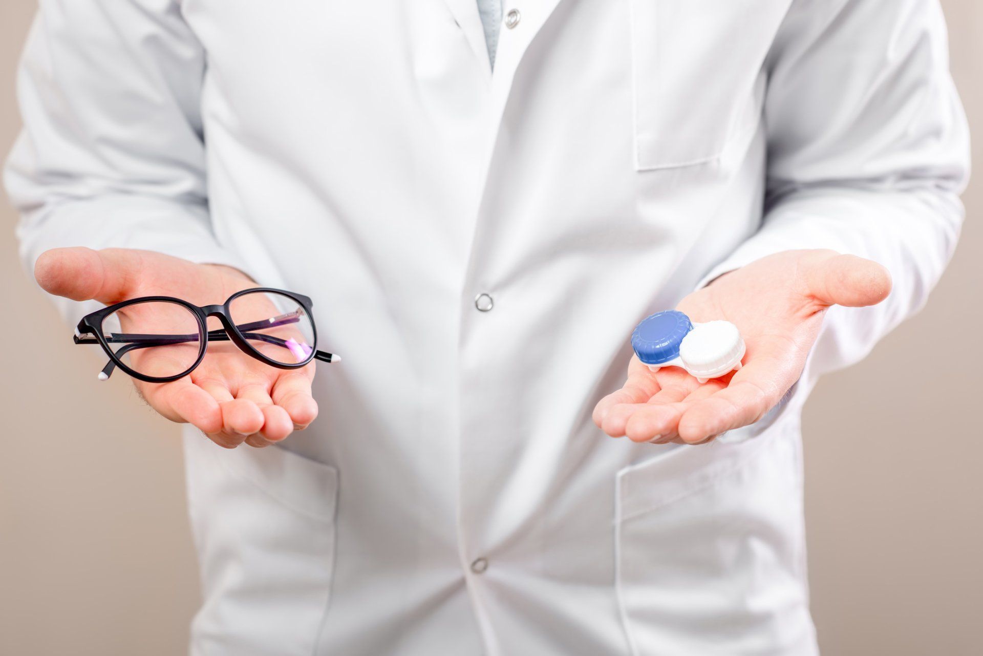 Person in white coat holding eyeglasses and contact lens case.