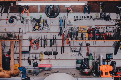 Una pared de taller abarrotada de herramientas colgadas, estantes y equipos eléctricos de color naranja.