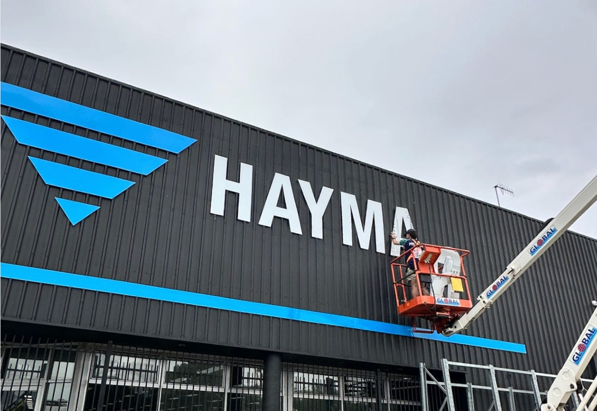 Construction Worker in an Aerial Lift Installing the HAYMA Sign — Millard Signs in Bungalow, QLD