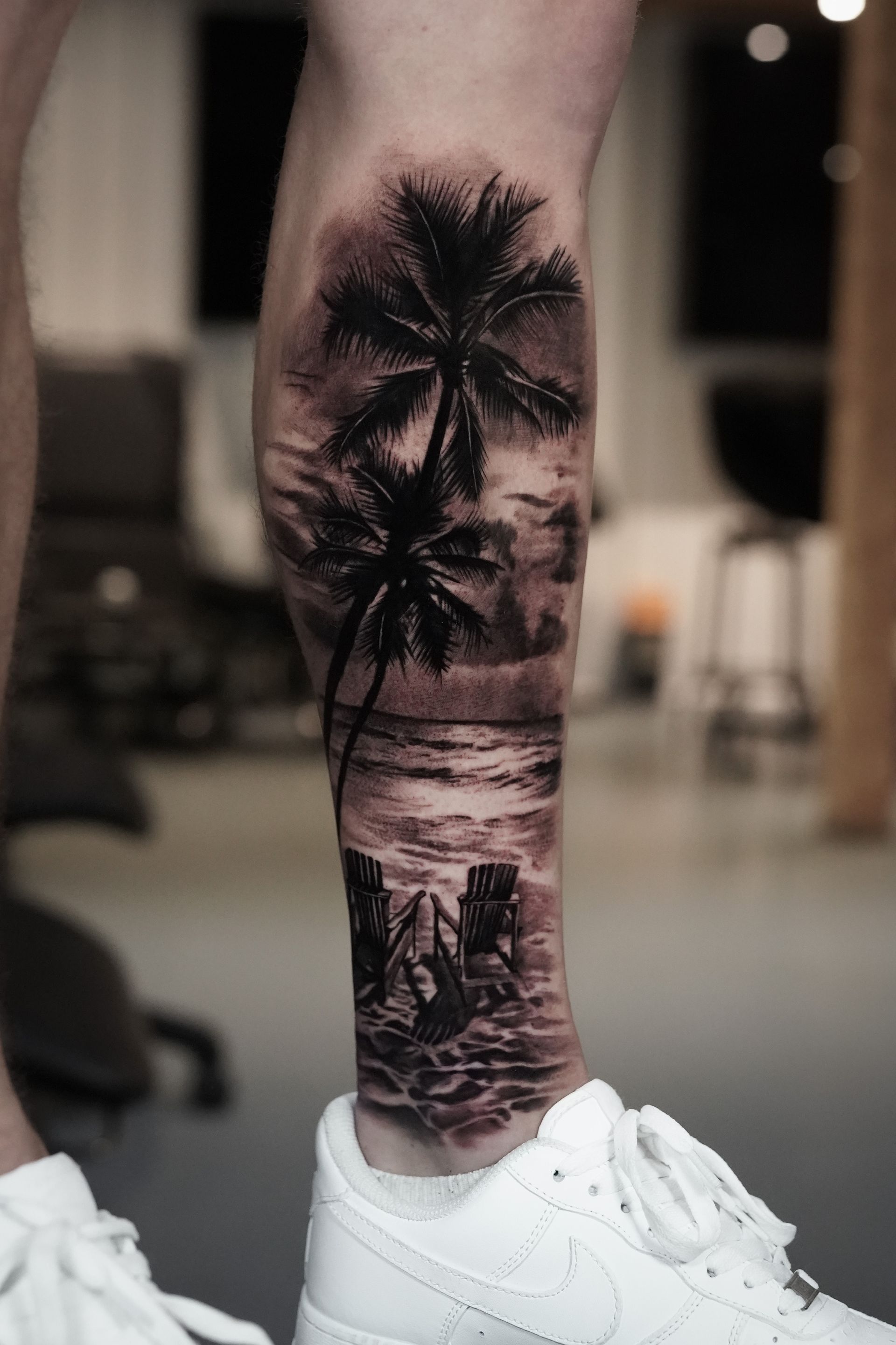 A person has a tattoo of palm trees on their leg.