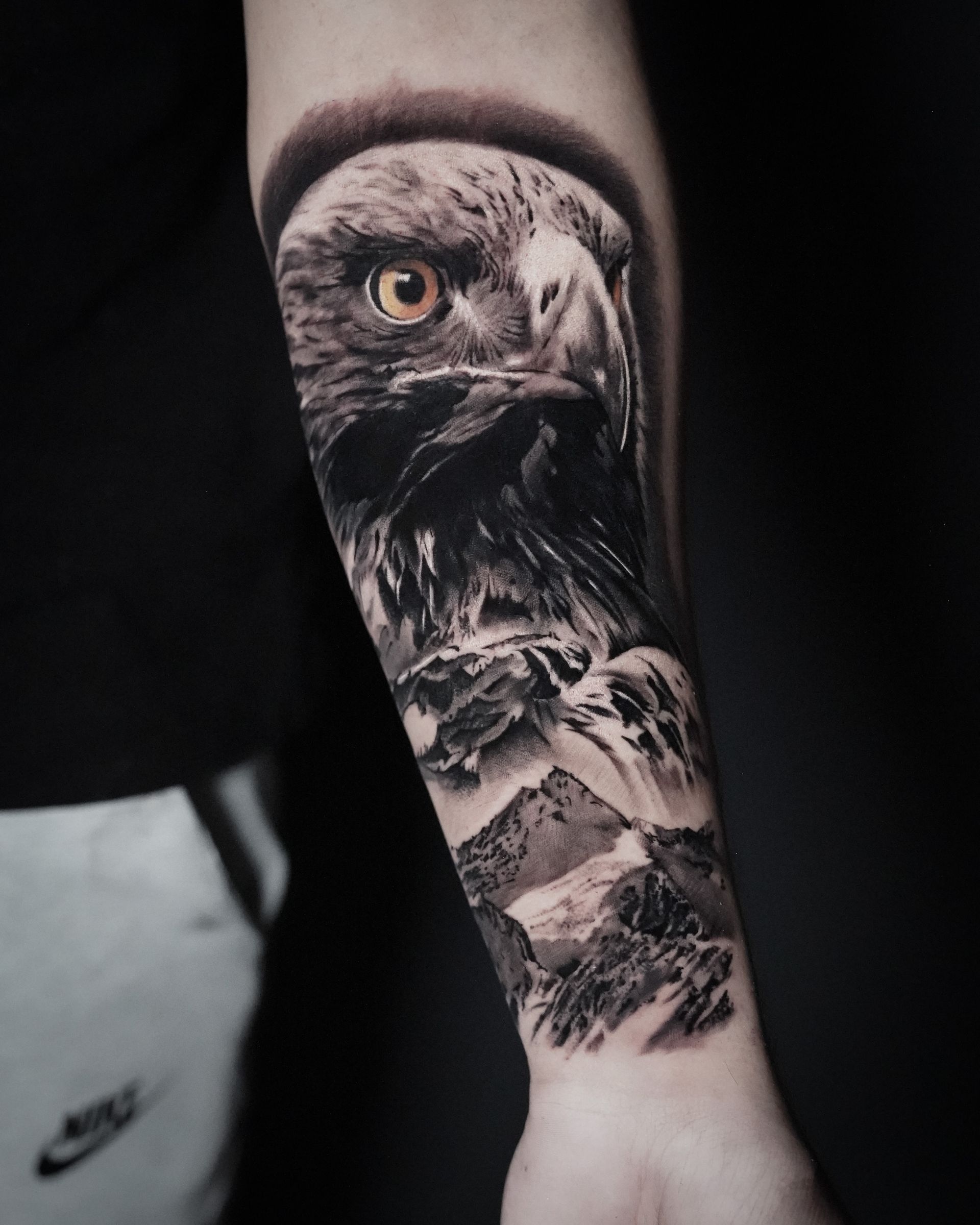 A man has a tattoo of an eagle and mountains on his forearm.