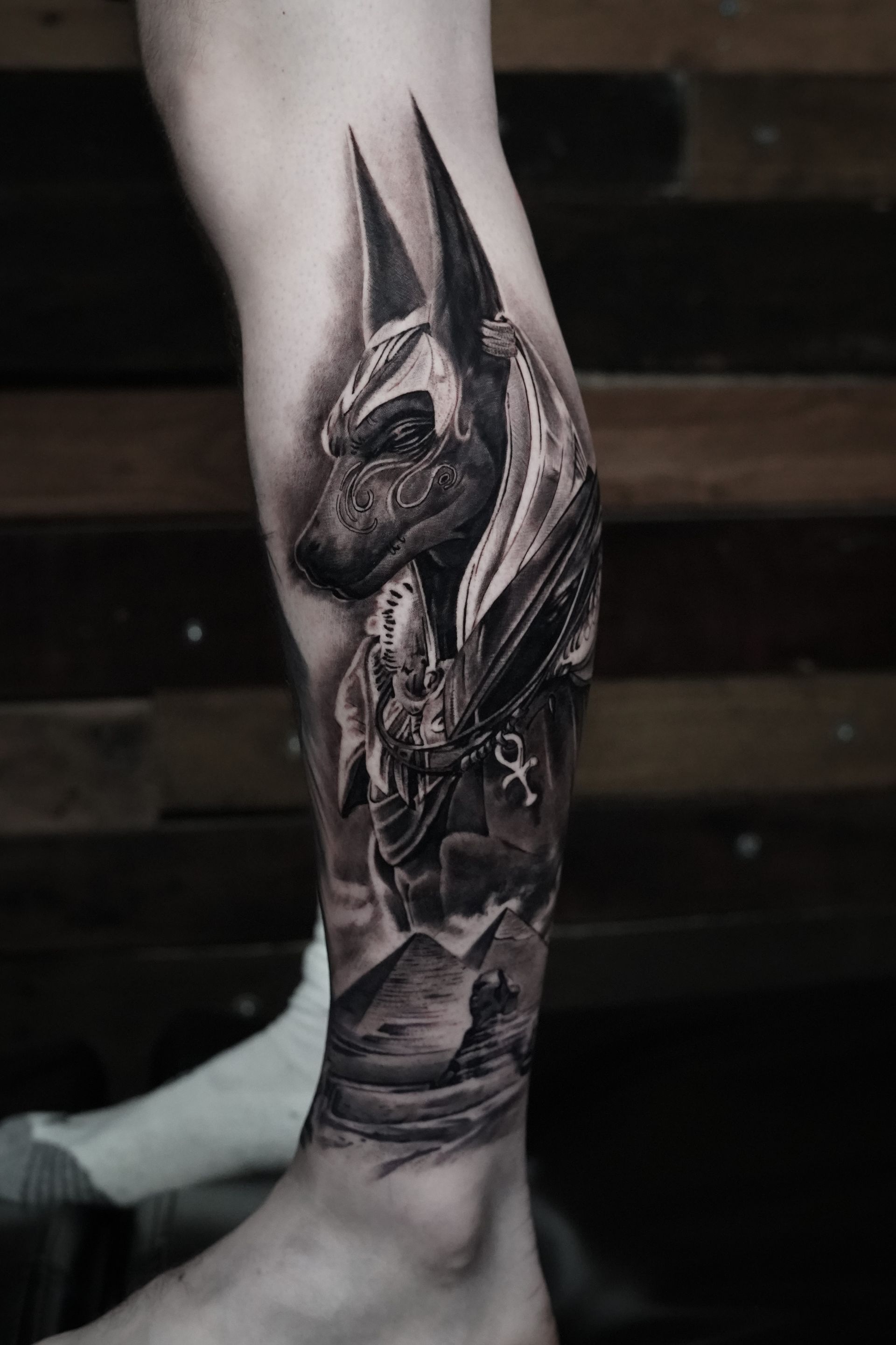 A black and white tattoo of anubis on a person 's leg.