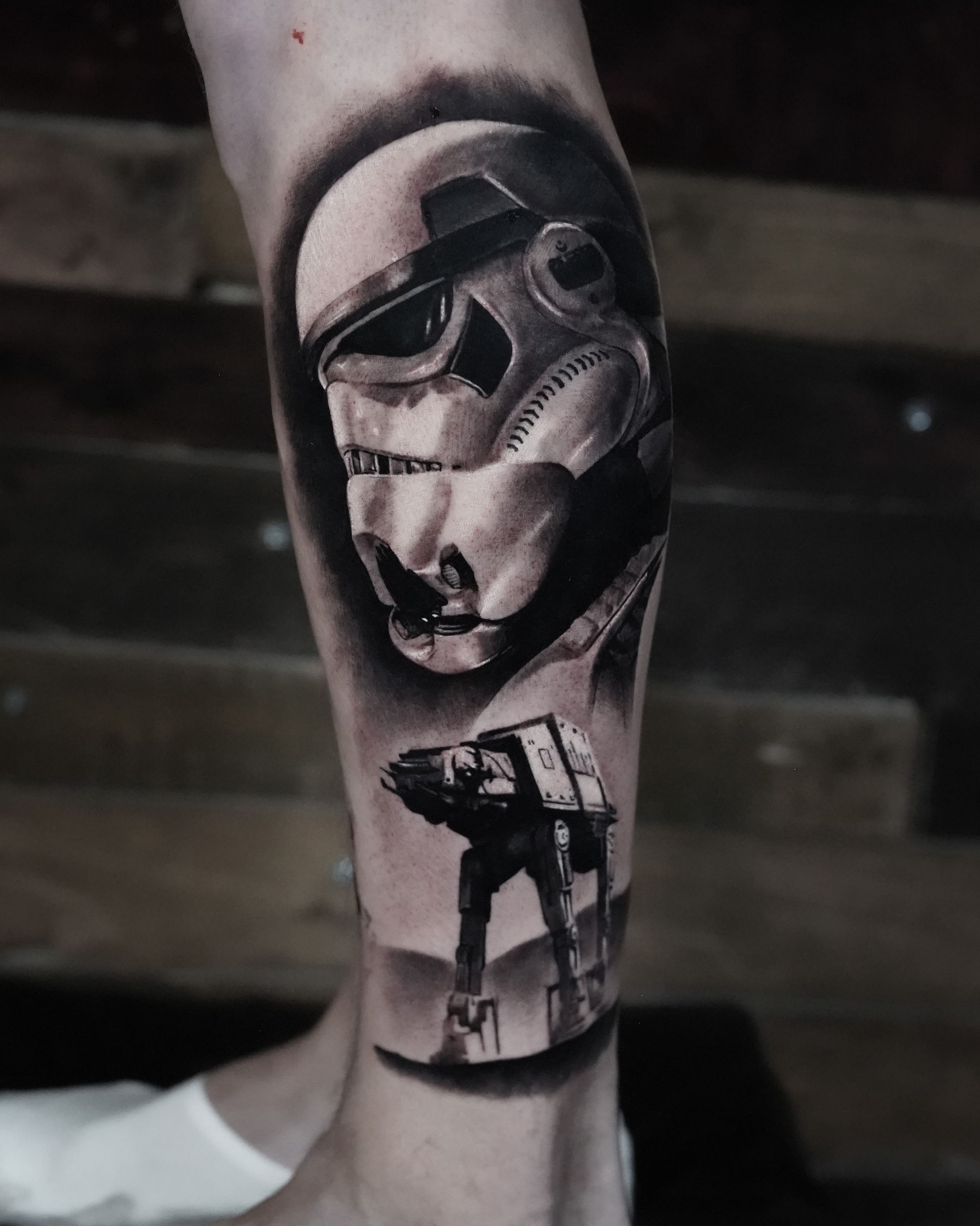 A black and white tattoo of a storm trooper and at at on a leg.