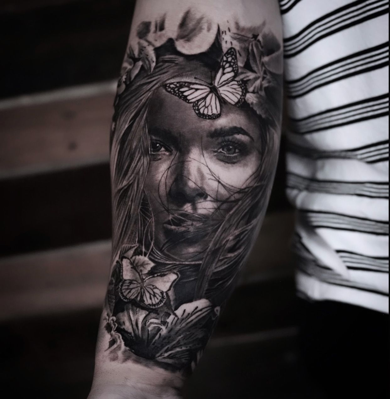 A black and white tattoo of a woman 's face with butterflies on her head.