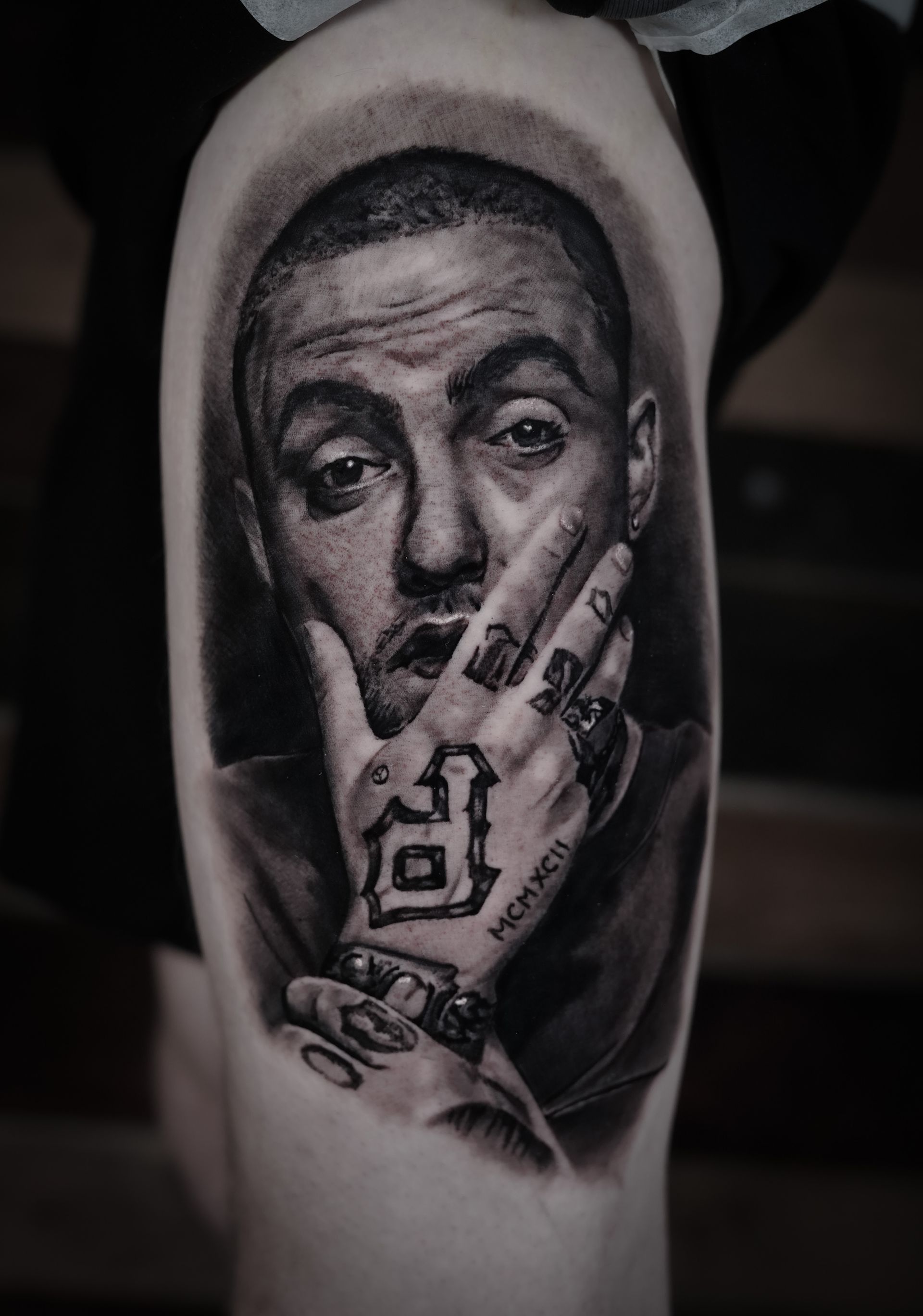 A black and white tattoo of a man covering his mouth with his hand.