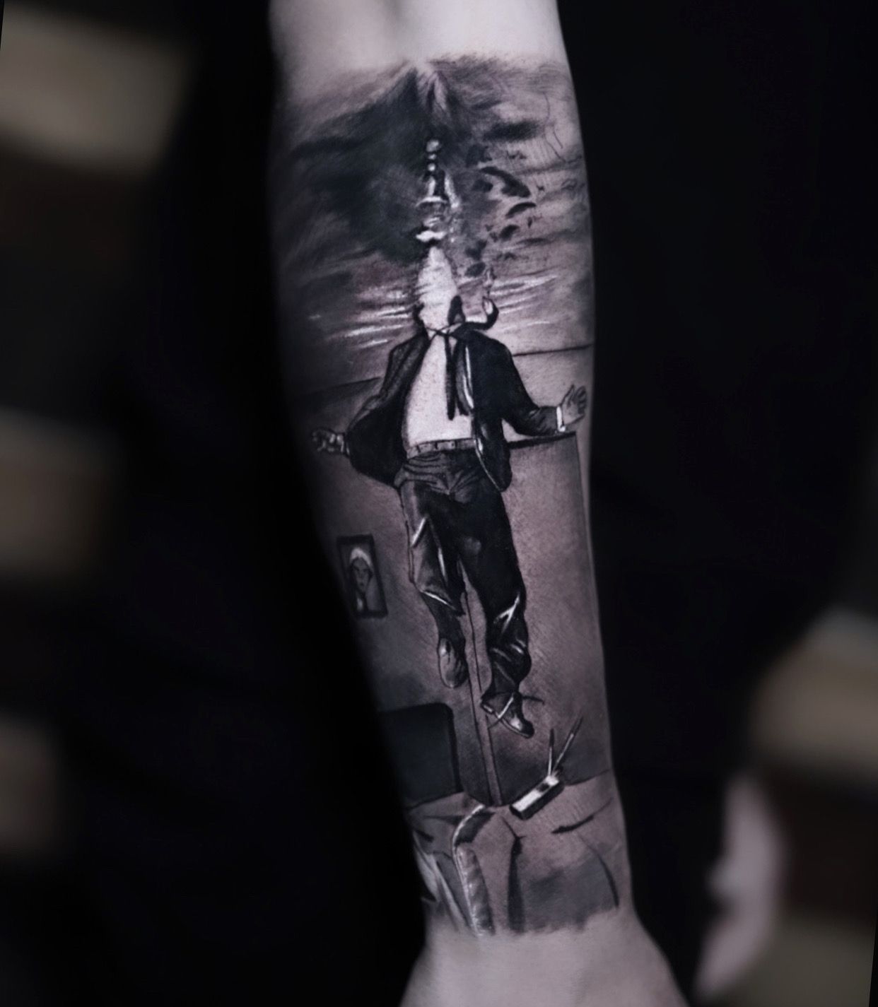 A black and white tattoo of a man in a suit and tie on a forearm.