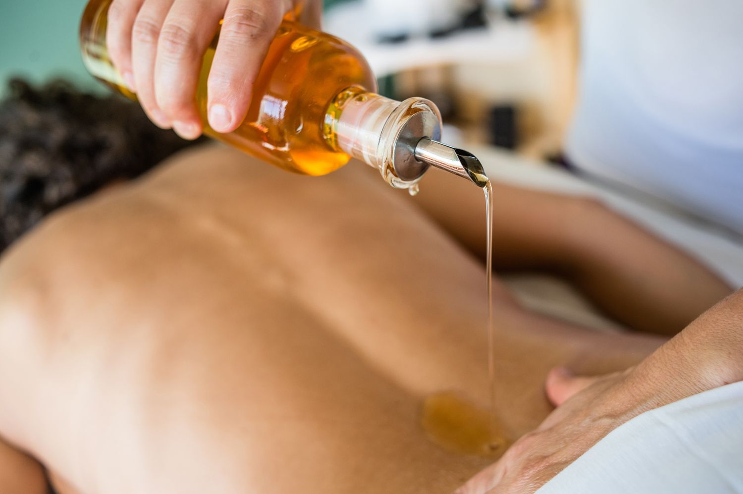 Massage therapist pouring oil onto a client's back during a spa treatment