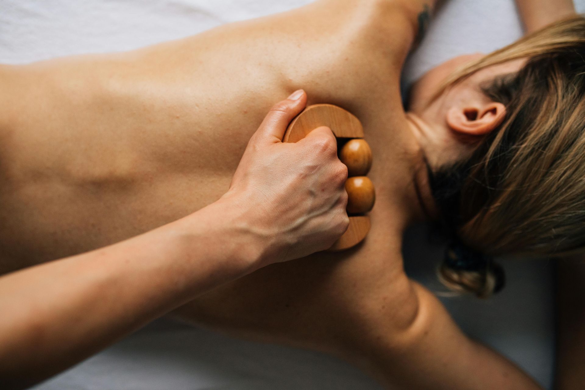 Massage therapist using wooden massage balls on a person’s back and neck