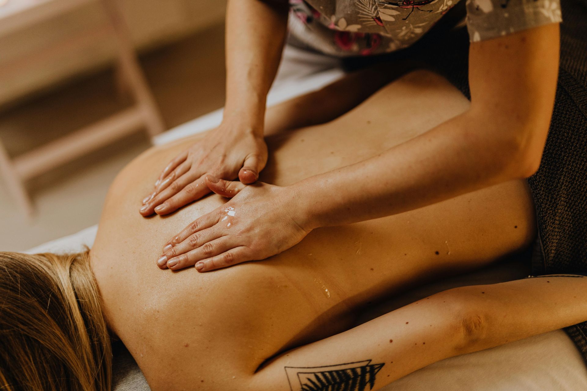 Hands massage a person’s back on a spa table.