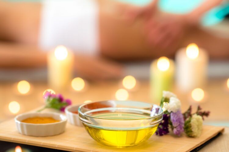 Oil bowls with flowers and lit candles on a wooden tray in a spa setting