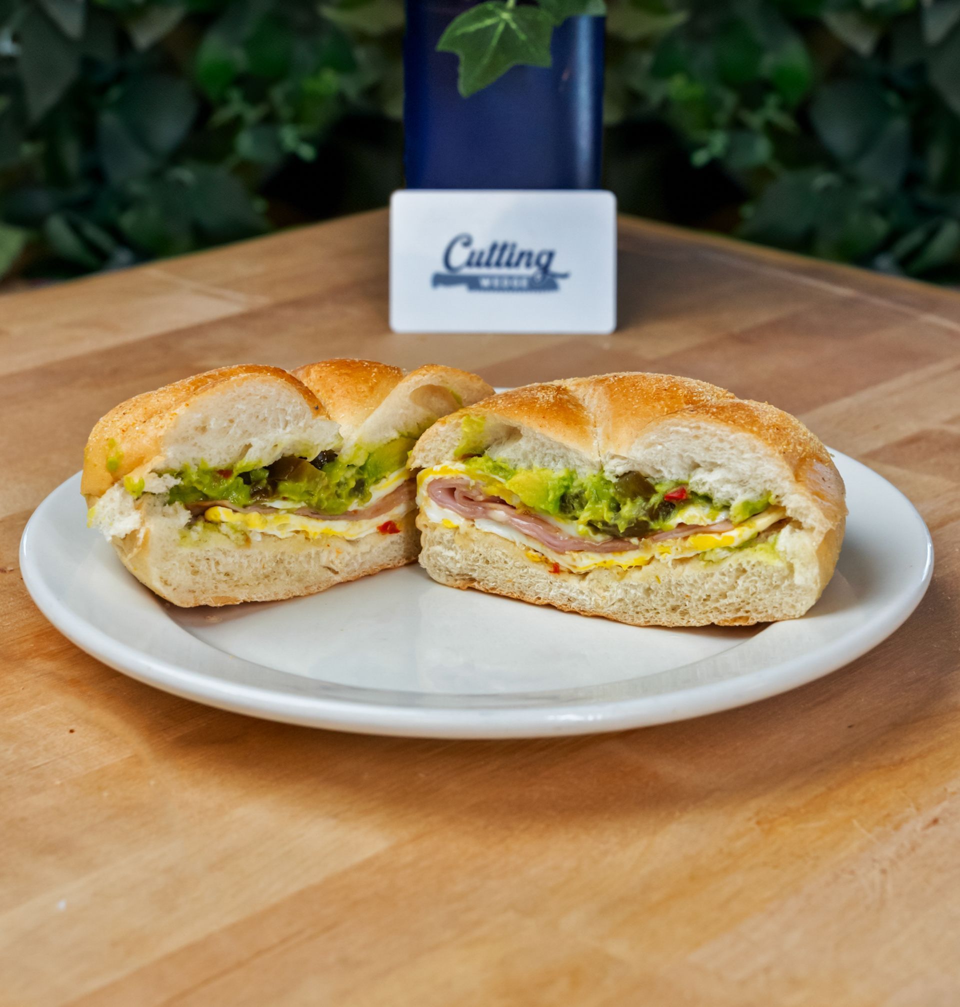 A sandwich is cut in half on a white plate on a wooden table.