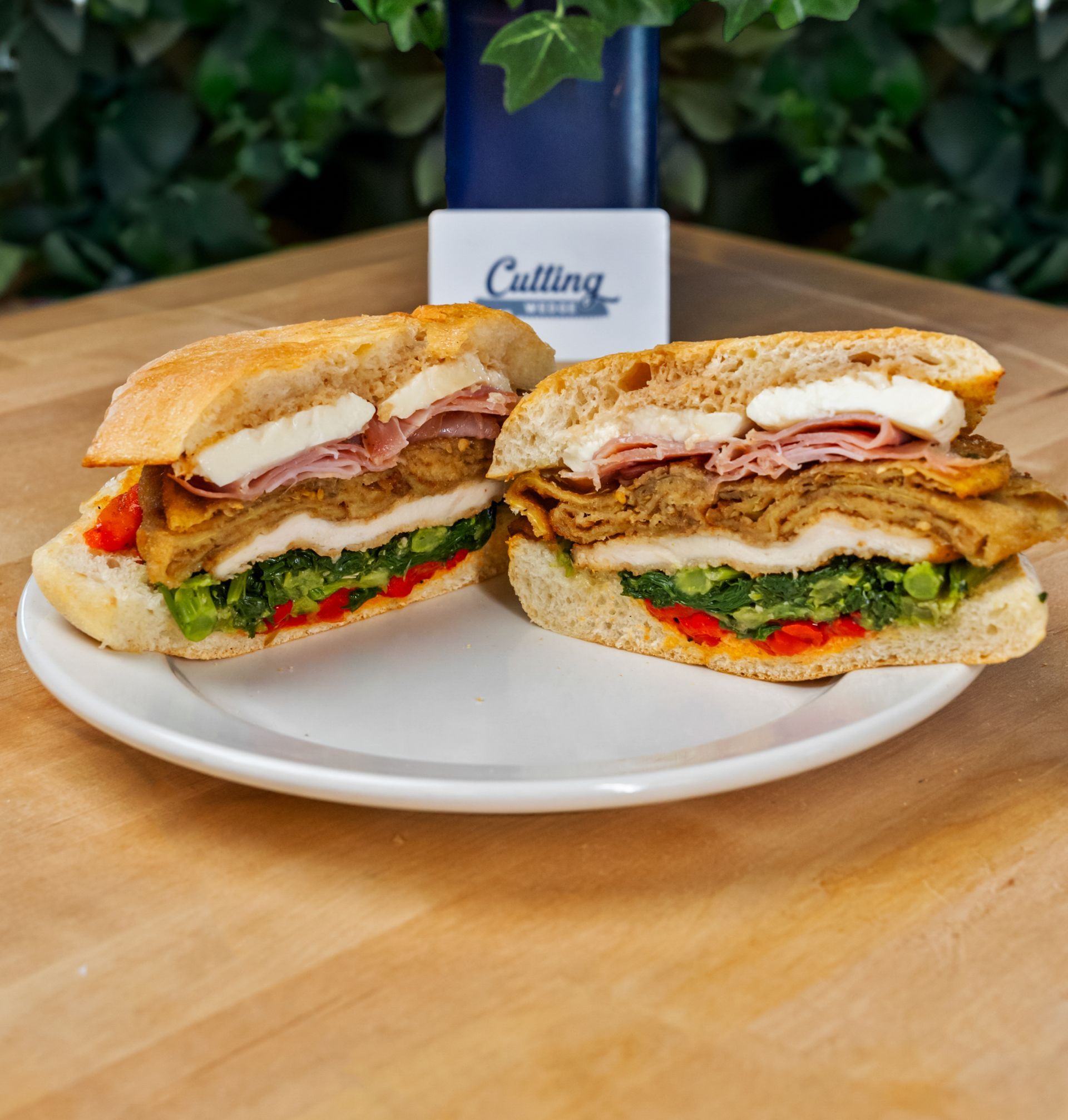 Two sandwiches are cut in half on a white plate on a wooden table.