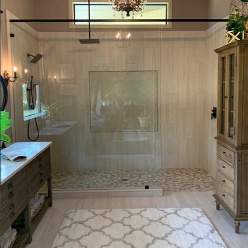 A bathroom with a walk in shower , sink , mirror and rug.