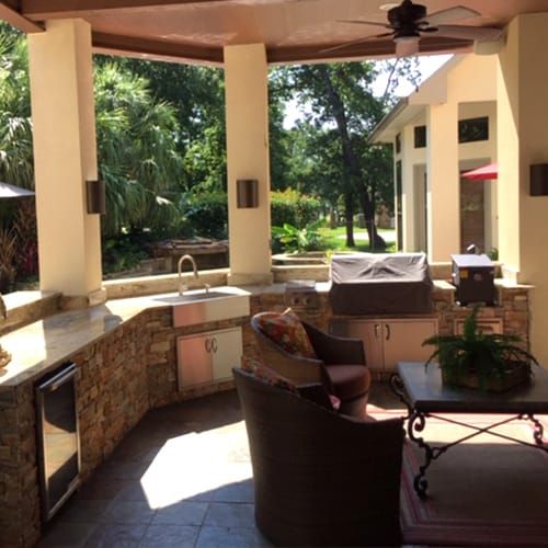A patio with a grill , chairs , a table and a ceiling fan.