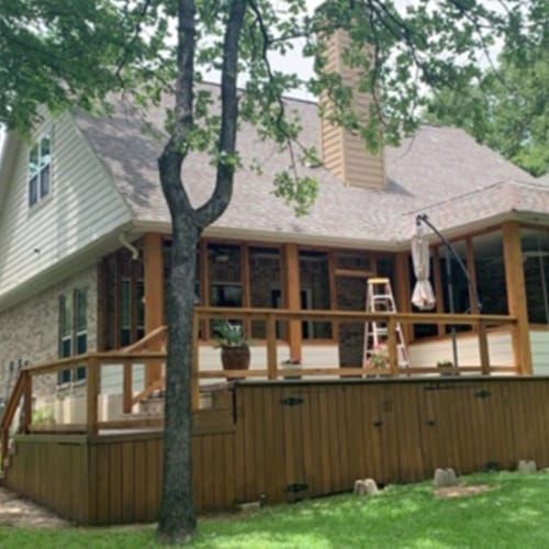 A house with a large deck and a tree in front of it.