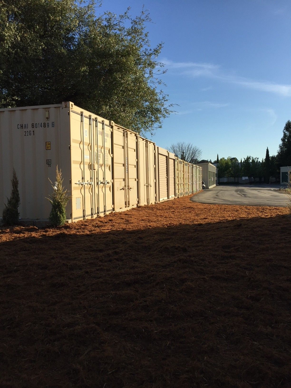 A row of shipping containers are lined up along a dirt road