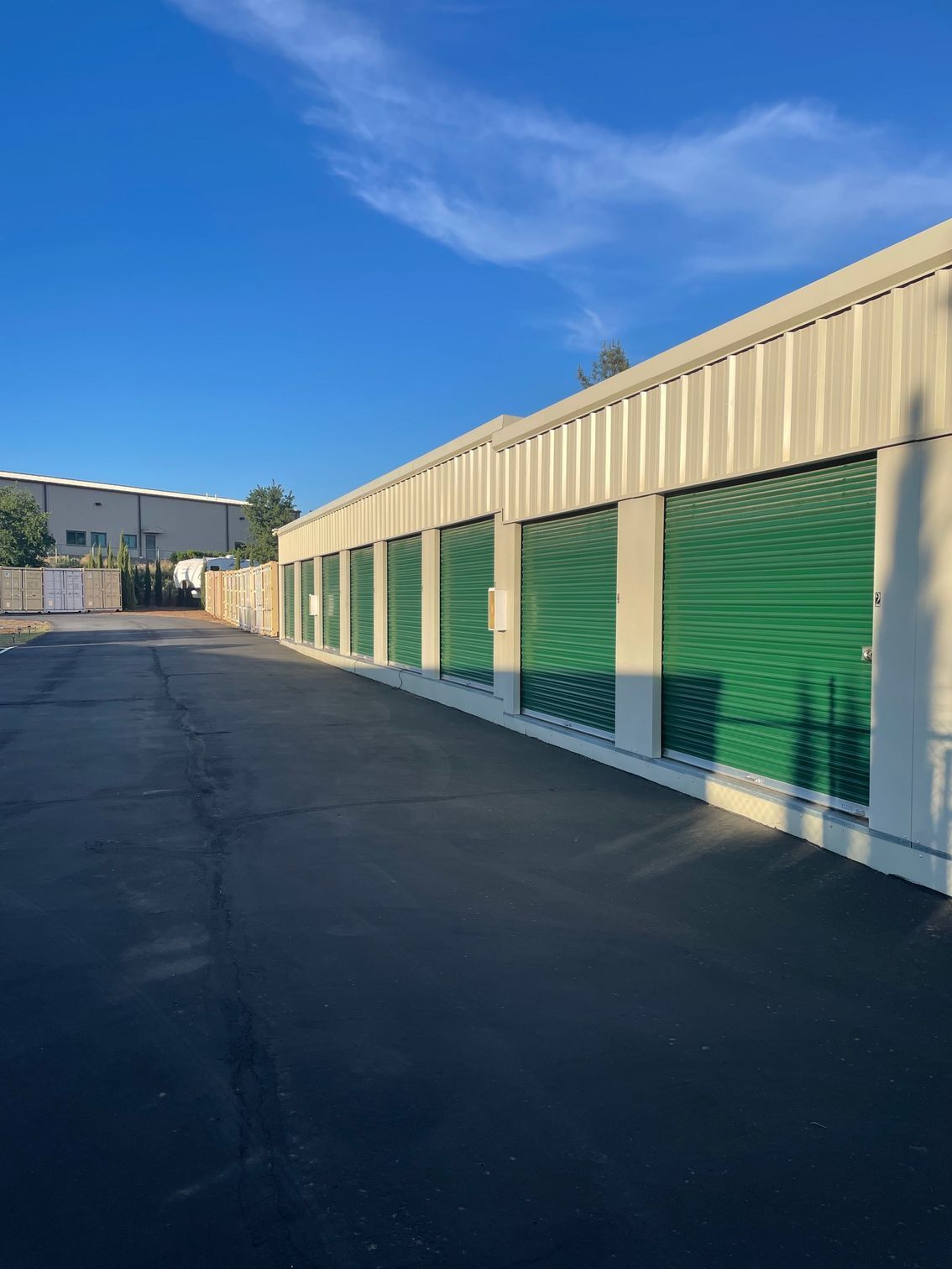 A row of storage units with green doors on a sunny day.