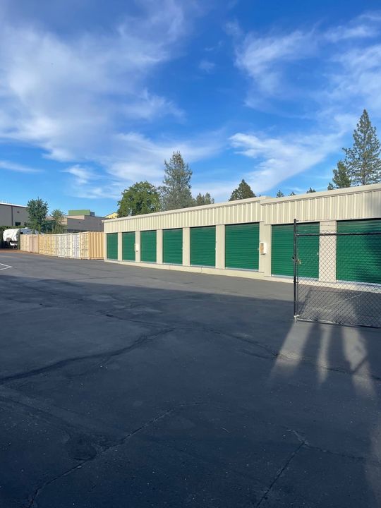 A row of green storage units are lined up in a parking lot.