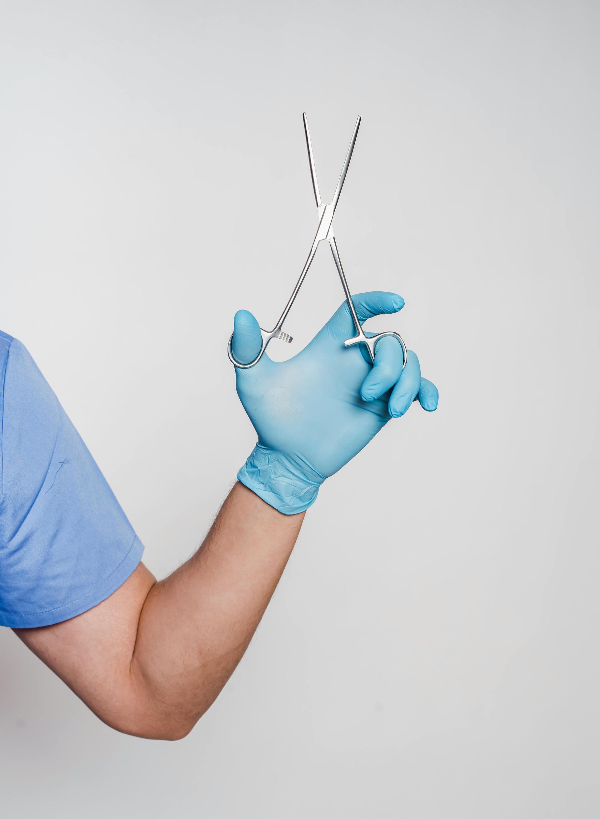 A person wearing blue gloves is holding a pair of scissors.