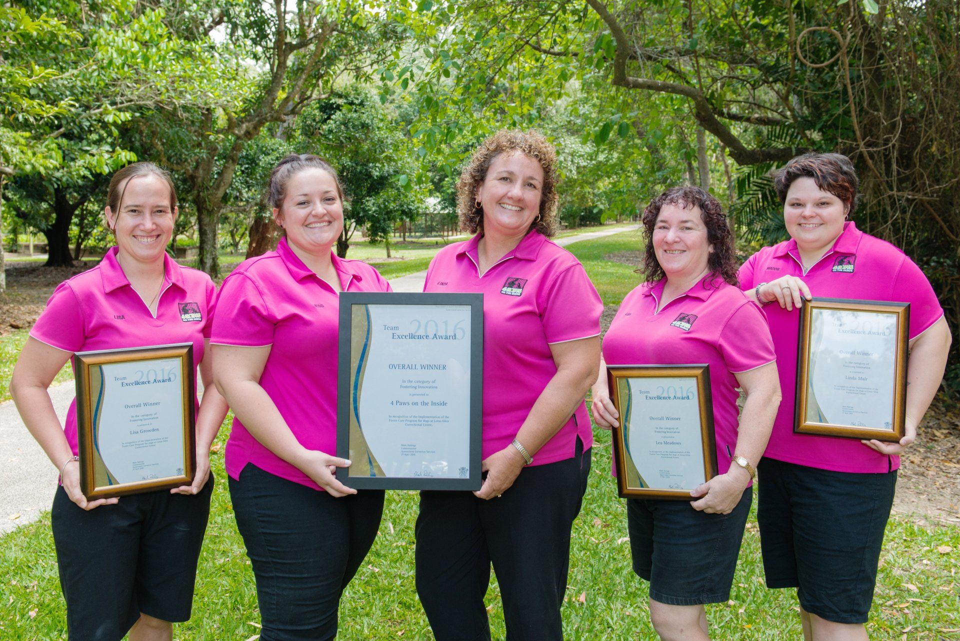 A Group Of Women In Pink Shirts Are Holding Framed Certificates — Canine Training School In Cairns, QLD