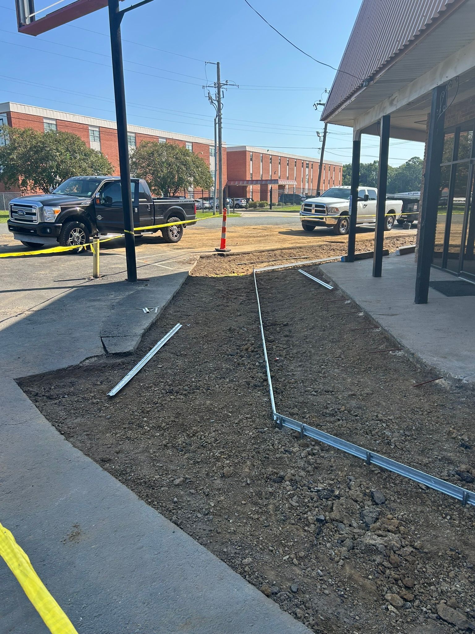Construction site with dark gravel, yellow caution tape, and vehicles near a building.