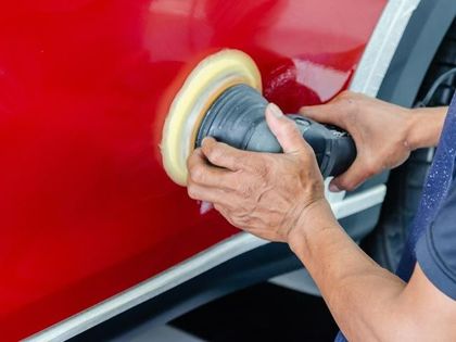 A man is polishing a red car with a polisher.