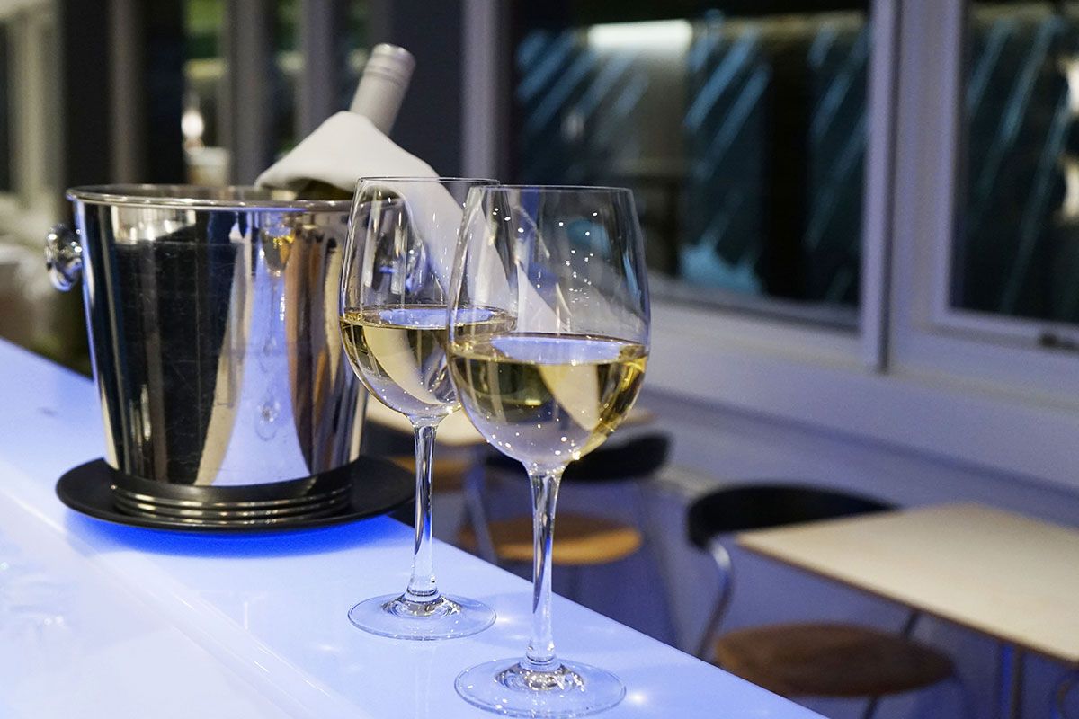 To vinglas fyldt med hvidvin på en bar, med en vinflaske i en isspand.