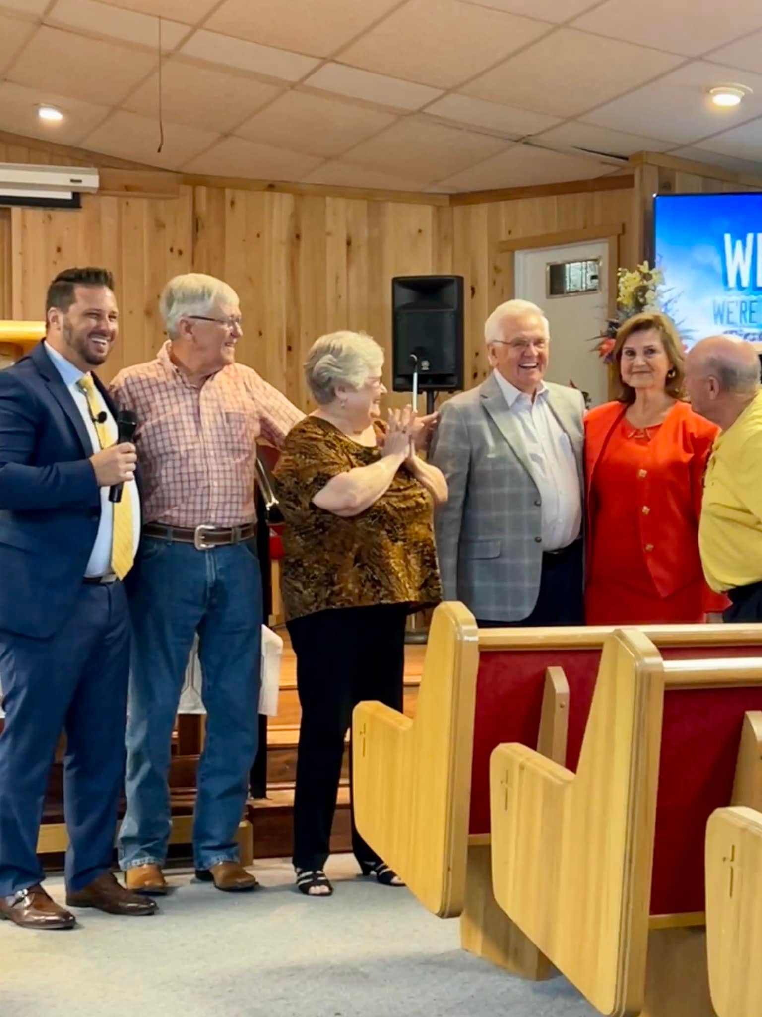 Group of people in a church, smiling and posing. Wooden interior.