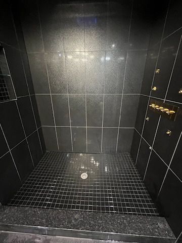 A bathroom with black tiles and a walk in shower.
