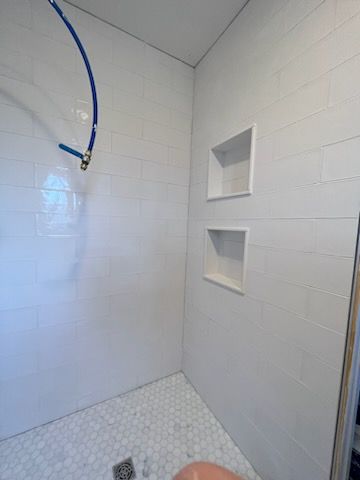 A shower with a hose hanging from the ceiling and two shelves.