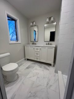 A bathroom with two sinks , a toilet , and a window.