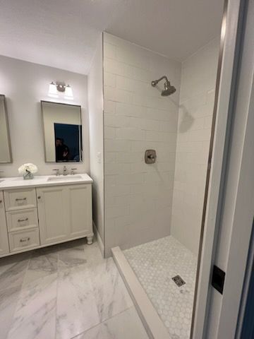 A bathroom with a walk in shower , sink and mirror.
