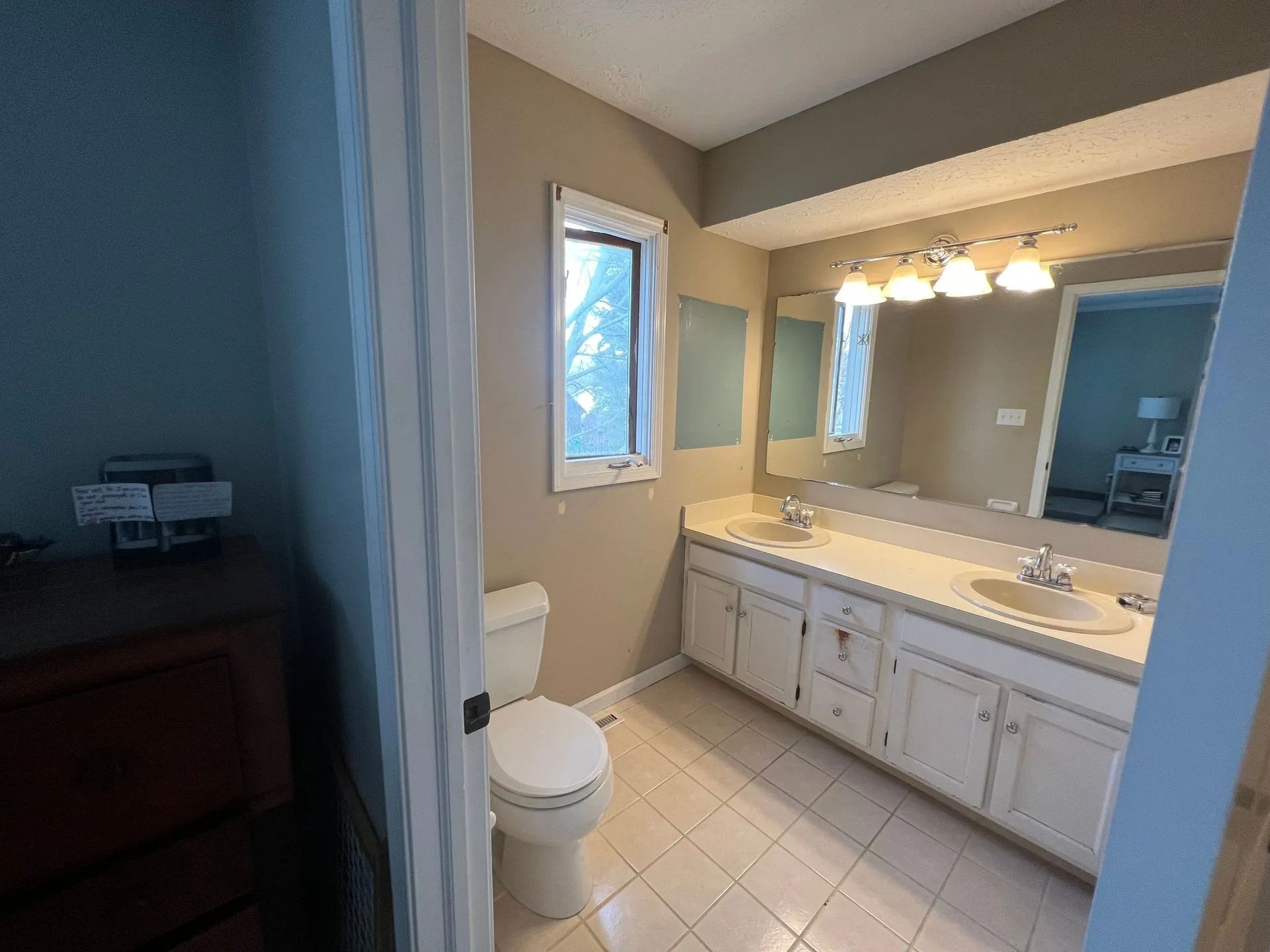 Bathroom with white vanity, toilet, and window; beige walls.