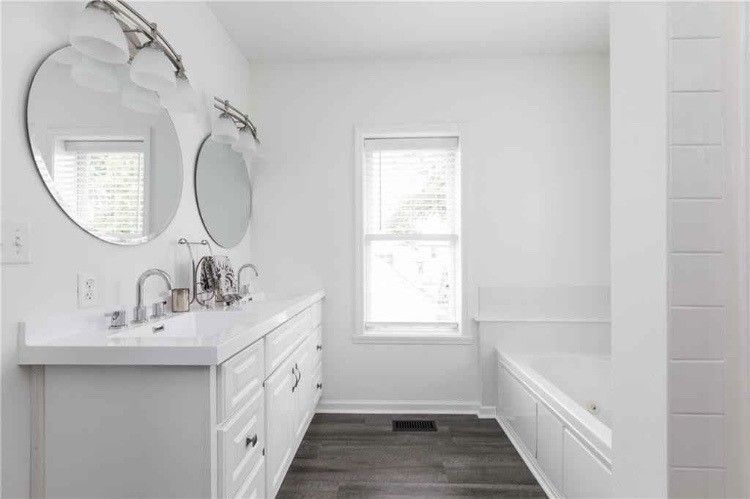 A bathroom with two sinks , two mirrors and a tub.