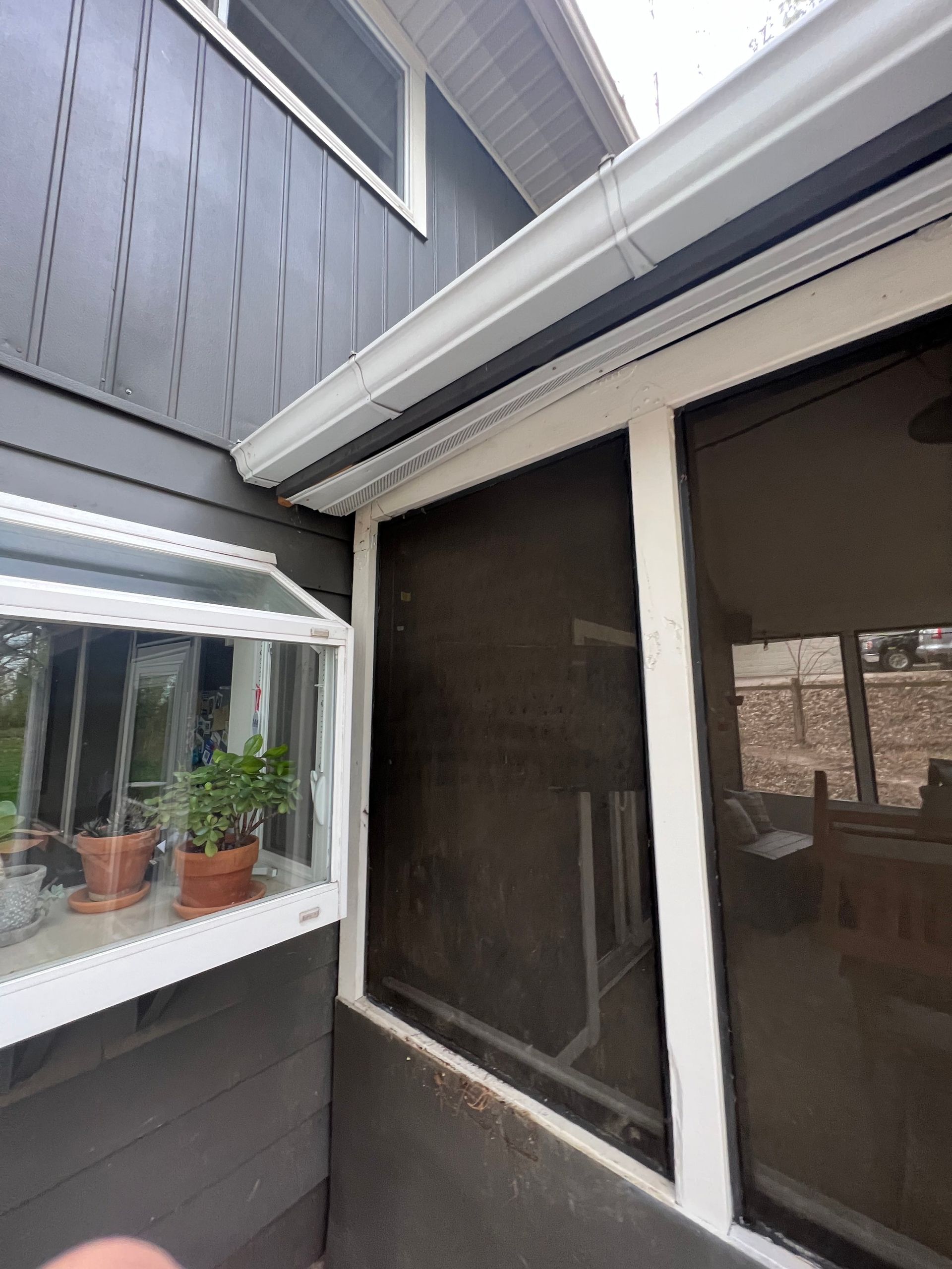A screened in porch with potted plants on the window sill