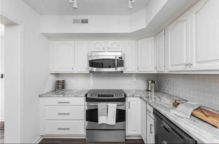 A kitchen with white cabinets , a stove , a microwave , and a dishwasher.