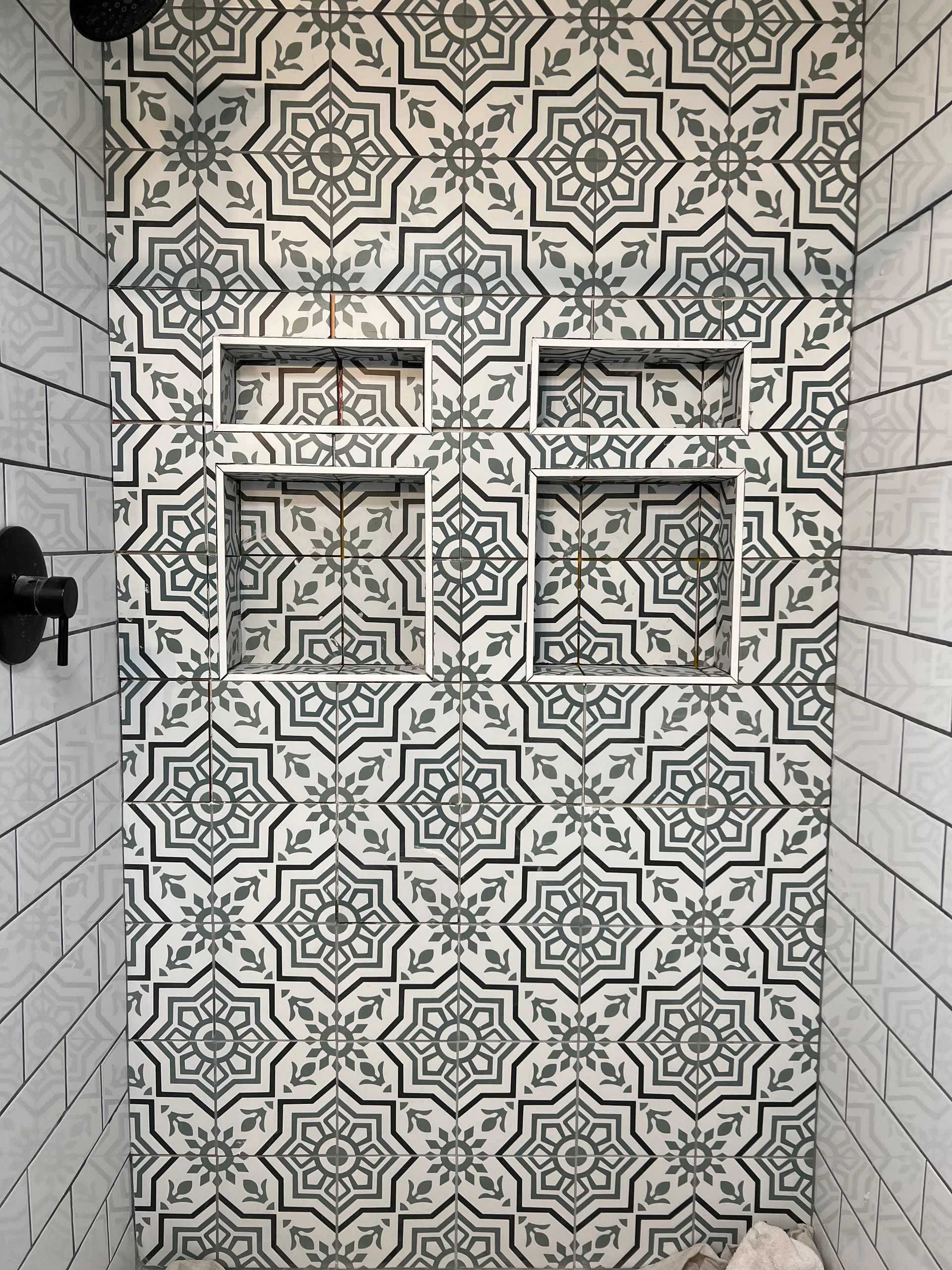 A shower with a black and white tile wall and two shelves.