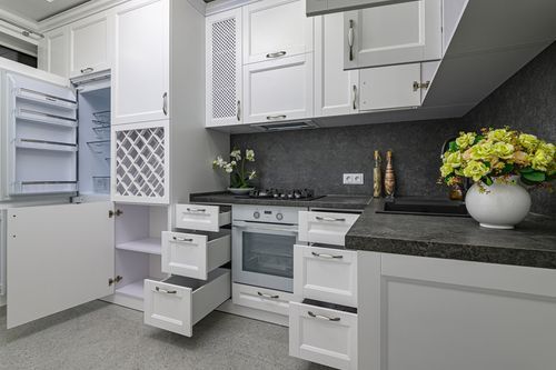 A kitchen with white cabinets , a refrigerator , a stove , and a vase of flowers.