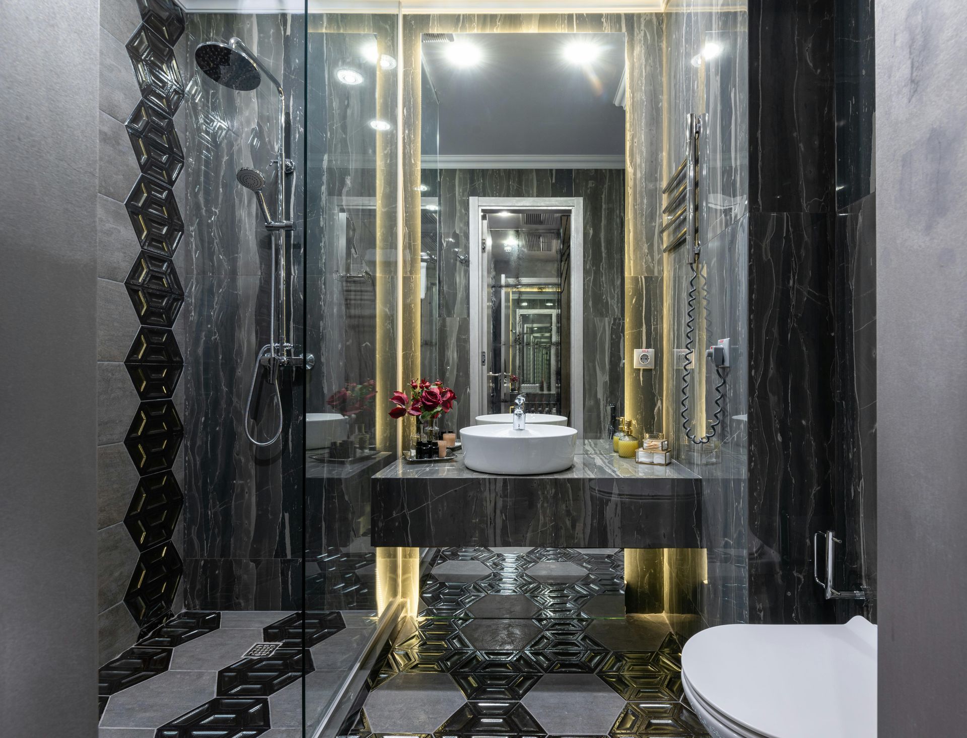 Modern bathroom with dark marble walls, a glass-enclosed shower, a floating vanity with a vessel sink, and gold accents.