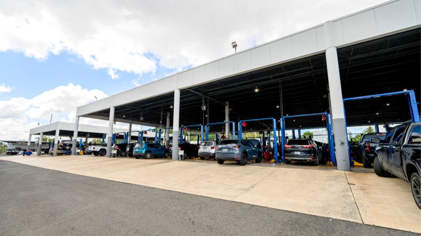 Exterior of auto repair shop with multiple bays, cars on lifts, under a blue sky in Puerto Rico.